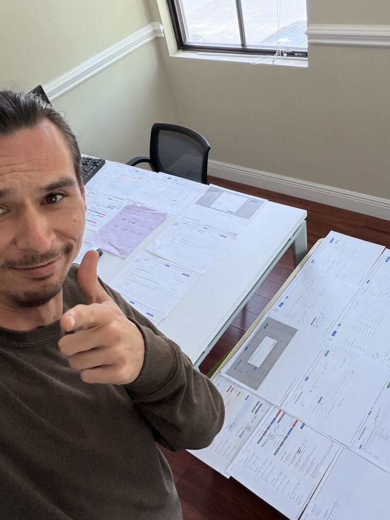 A Mission Grant team member at a desk covered in printed Google Ads campaign and analytics reports, giving a thumbs up to the camera.